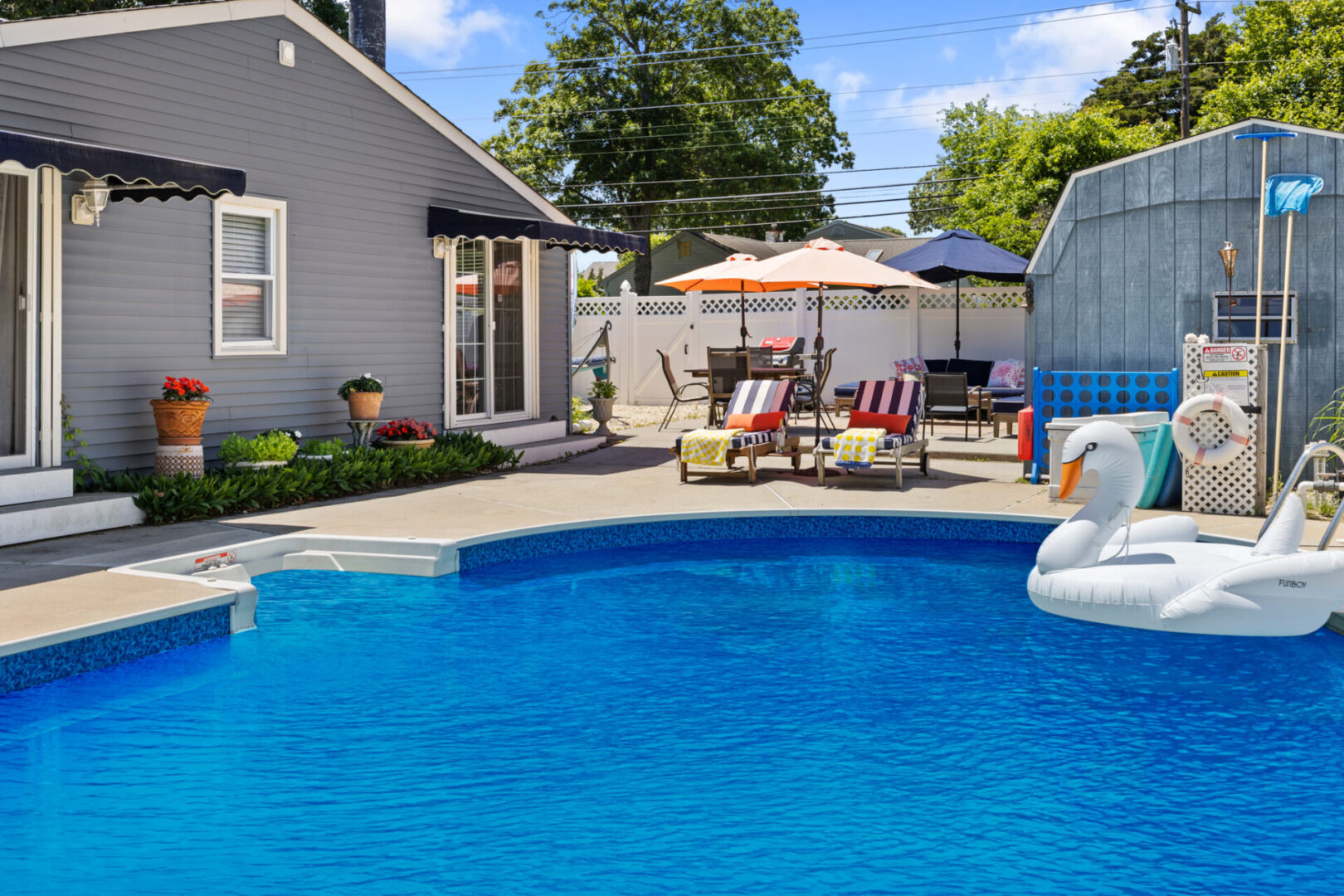 Sunny backyard with a clear blue pool and lounge chairs under umbrellas.