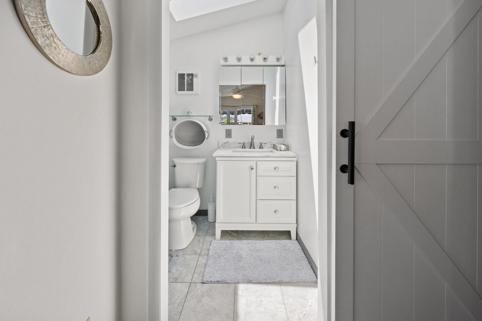 Bright, modern bathroom with white cabinetry and a round mirror.