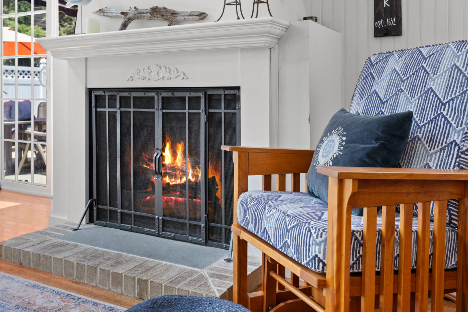 Cozy living room fireplace with wooden chair and blue cushions.
