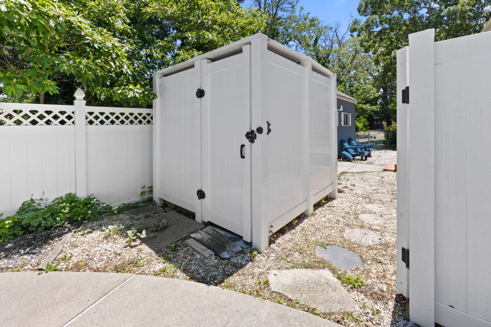 A white storage shed with double doors in a backyard.