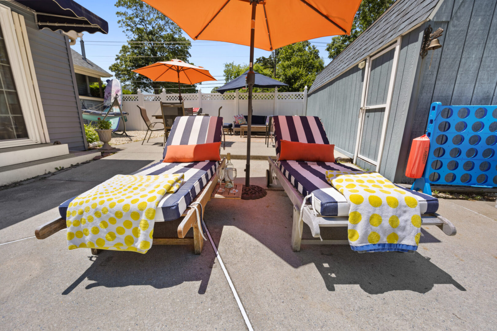 Two lounge chairs with yellow towels and orange umbrellas on a sunny patio.